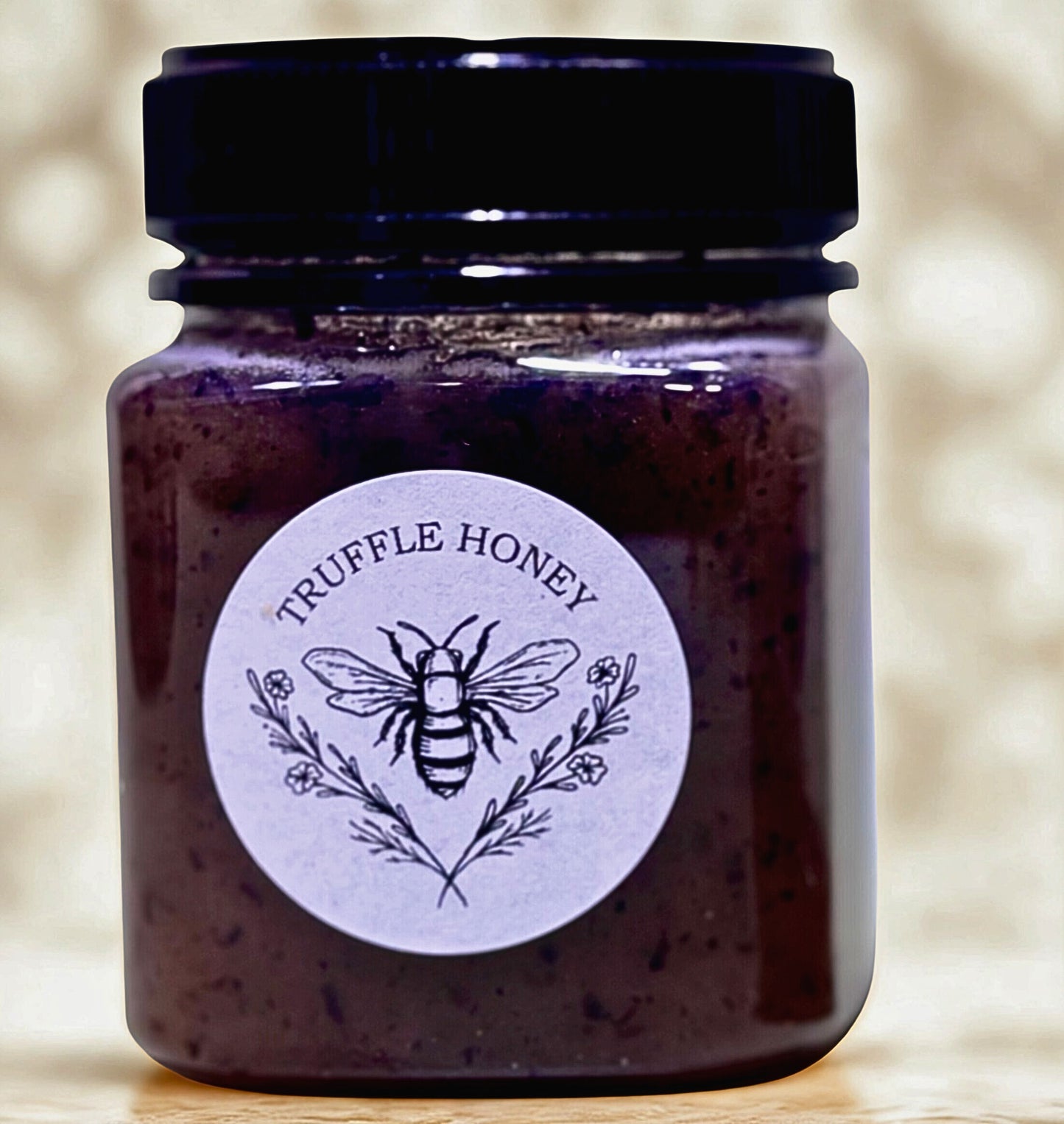 Jar of truffle honey with a label featuring a bee and floral elements on a blurred background.